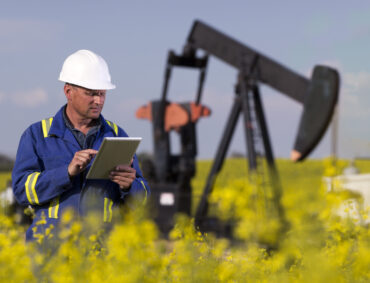 An image from the oil and gas industry of an oil worker using a tablet PC in front of a pumpjack.